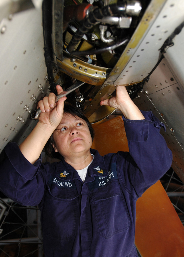 Eine weibliche Flugtechnikerin in einer blauen Uniform inspiziert oder repariert ein Flugzeug, während sie ein Werkzeug hält.