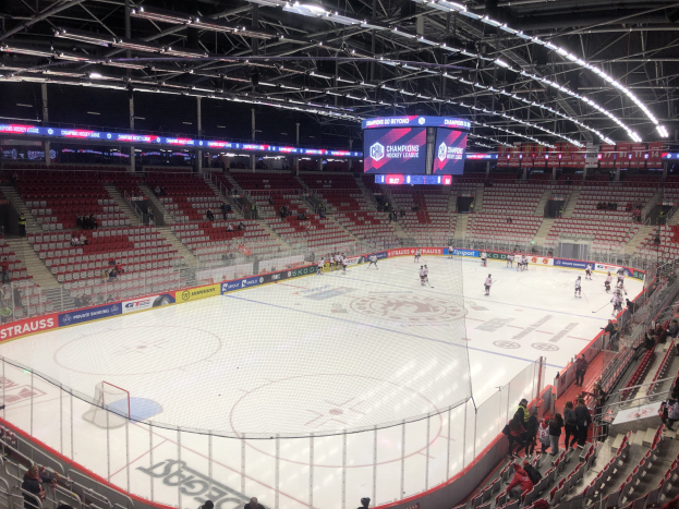 Eishockeyspiel in einer großen Arena zwischen den St. Louis Blues und Detroit Red Wings, mit Zuschauern auf den Sitzplätzen und Stehplätzen in der Nähe des Spielfelds, umgeben von einem Zaun, einem Anzeigebildschirm, Metallrahmen, Deckenleuchten und einem Dach.