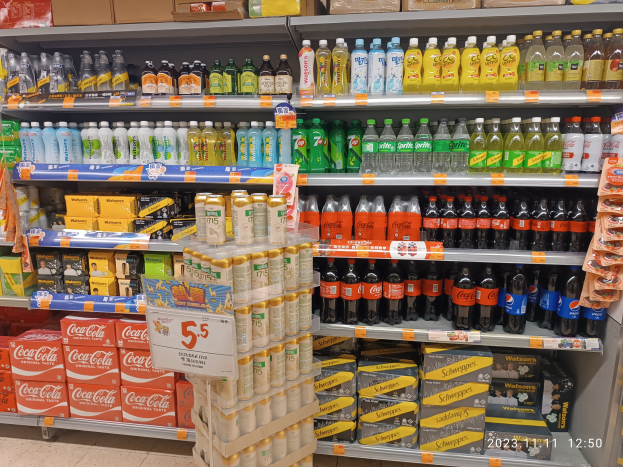 Ein gut gefülltes Regal mit verschiedenen Getränken in Flaschen, Kartons und anderer Verpackung, mit einem sichtbaren Boden und einem Text in der rechten unteren Ecke, der auf eine kostenlose Getränkeaktion bei Walmart hinweist.