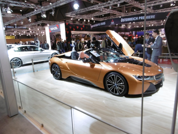 Ein glänzender schwarzer BMW i8 Roadster mit Chromakzenten auf der Internationalen Automobil-Ausstellung in Frankfurt umgeben von formell gekleideten Gästen.