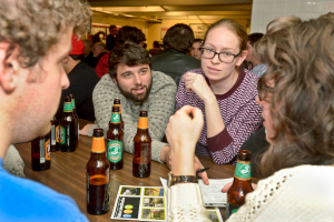 Mehrere Personen auf beiden Seiten eines Tisches mit Bierflaschen in einem Ort, der wie eine Bar aussieht.