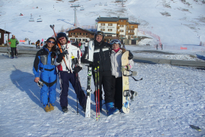 Vier Personen posieren mit Skaterpads und Werkzeugen vor einer schneebedeckten Berglandschaft.