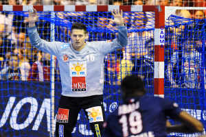 Handballspieler mit erhobenen Händen vor einem Tor, umgeben von Zuschauern bei der Futsal-Weltmeisterschaft 2019, mit einem Banner und Netz im Bild.