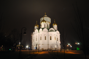 Die Kathedrale des Erlöserblutes in Kiev, Ukraine, ein großes weißes Gebäude mit Fenstern und Türen, umgeben von Bäumen und Laternenmasten, mit einer Straße davor und einem dunklen Himmel im Hintergrund.