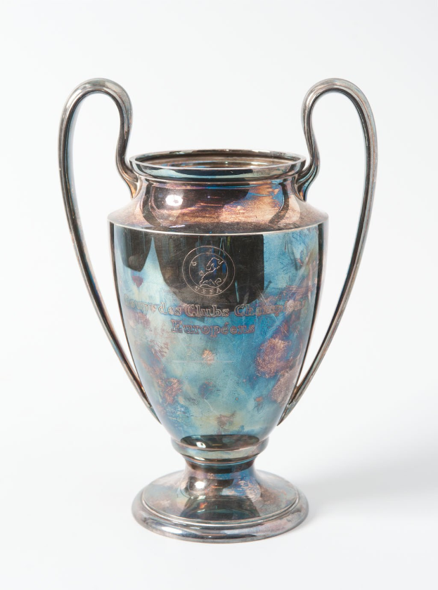 Der UEFA Champions League-Pokal, ein stahlerner Becher mit zwei Griffen, blauen und silbernen Akzenten und der Inschrift "UEFA Champions League", vor einem weißen Hintergrund.