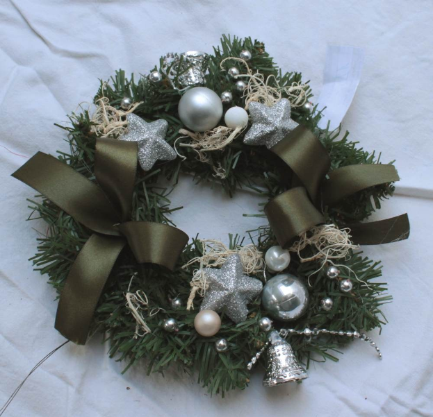 Ein festliches Weihnachtsgesteck mit silbernen Schmuckelementen und Bändern auf einem weißen Tuch, mit bunten Kugeln, Sternen und anderen Verzierungen.