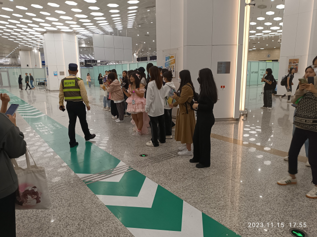 Menschen in der Schlange an einem Flughafen-Sicherheits-Check-in-Bereich, mit Taschen und Mobiltelefonen, mit Säulen und Deckenleuchten im Hintergrund.