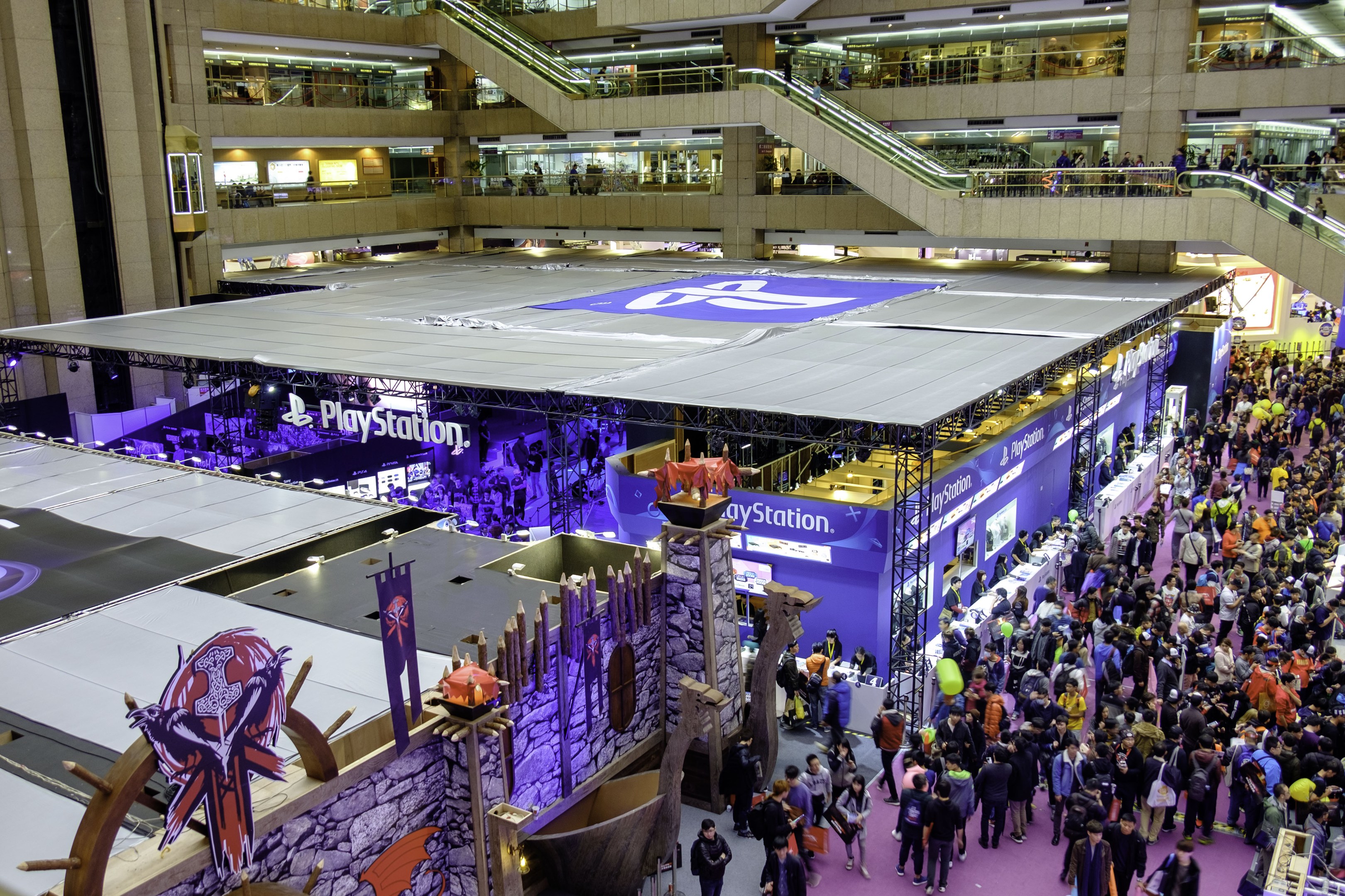 Eine große Menschenmenge in einem geräumigen Innenraum mit Rolltreppen, Geländern, beleuchteten Schildern, Bannern und anderen Anzeigen, die als die weltweit größte Gaming-Messe identifiziert werden.