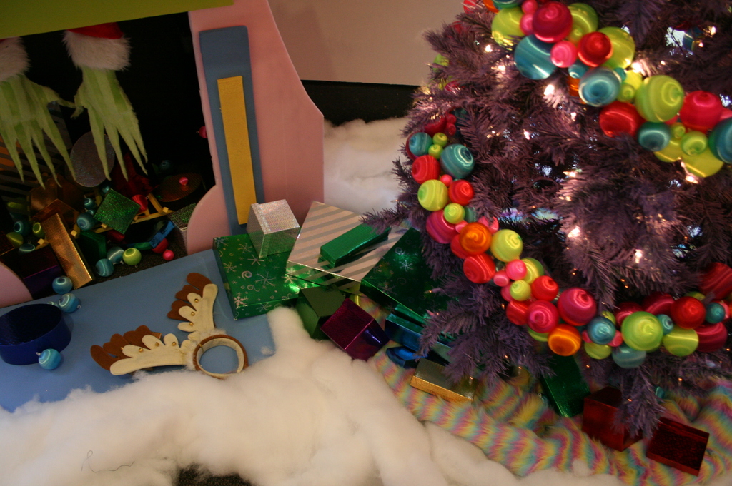 Drinnen steht rechts ein geschm√√∂kter Weihnachtsbaum mit Lichterketten und Schmuck, in der Mitte Geschenkboxen und Deko, oben links eine H√ľtte mit Deko und unten Wolle und Baumwolle.