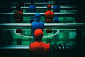 Ein buntes Tischfußballspiel mit einer Gruppe von Menschen in verschiedenenfarbigen Trikots, die mittelfeldpositioniert bereit sind, ein Tischfußballspiel zu starten.