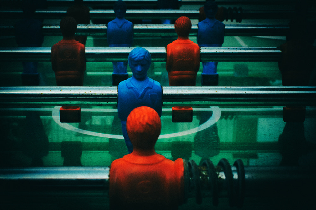 Ein buntes Tischfußballspiel mit einer Gruppe von Menschen in verschiedenenfarbigen Trikots, die mittelfeldpositioniert bereit sind, ein Tischfußballspiel zu starten.