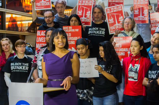 Eine Black-Lives-Matter-Aktivistin spricht an einem Podium mit Mikrofon zu einer Menge mit Schildern.