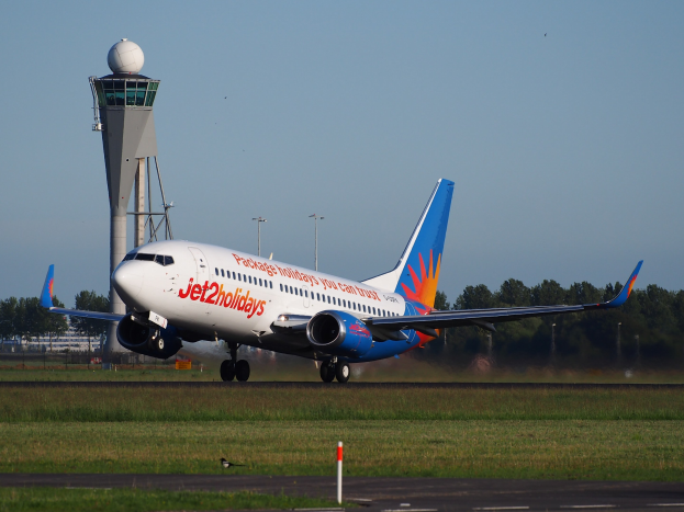 Ein Jet2holidays Airbus A320-200-Flugzeug startet vom Frankfurter Flughafen, umgeben von grünem Gras und einem hohen Turm, mit Bäumen und Gebäuden im Hintergrund unter einem klaren blauen Himmel.