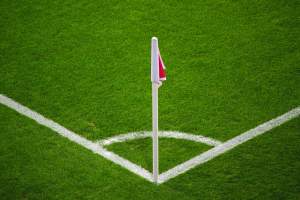 Ein Fußballfeld mit grünem Rasen, weißen Begrenzungslinien und einem weißen Pfahl mit einer roten und weißen Flagge in der Mitte des Elfmeterpunkts.