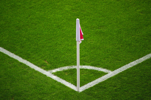 Ein Fußballfeld mit grünem Rasen, weißen Begrenzungslinien und einem weißen Pfahl mit einer roten und weißen Flagge in der Mitte des Elfmeterpunkts.
