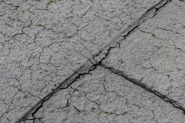 Nahaufnahme einer verwitterten Straße mit tiefen, breiten Rissen und einer rauen, unebenen Oberfläche.