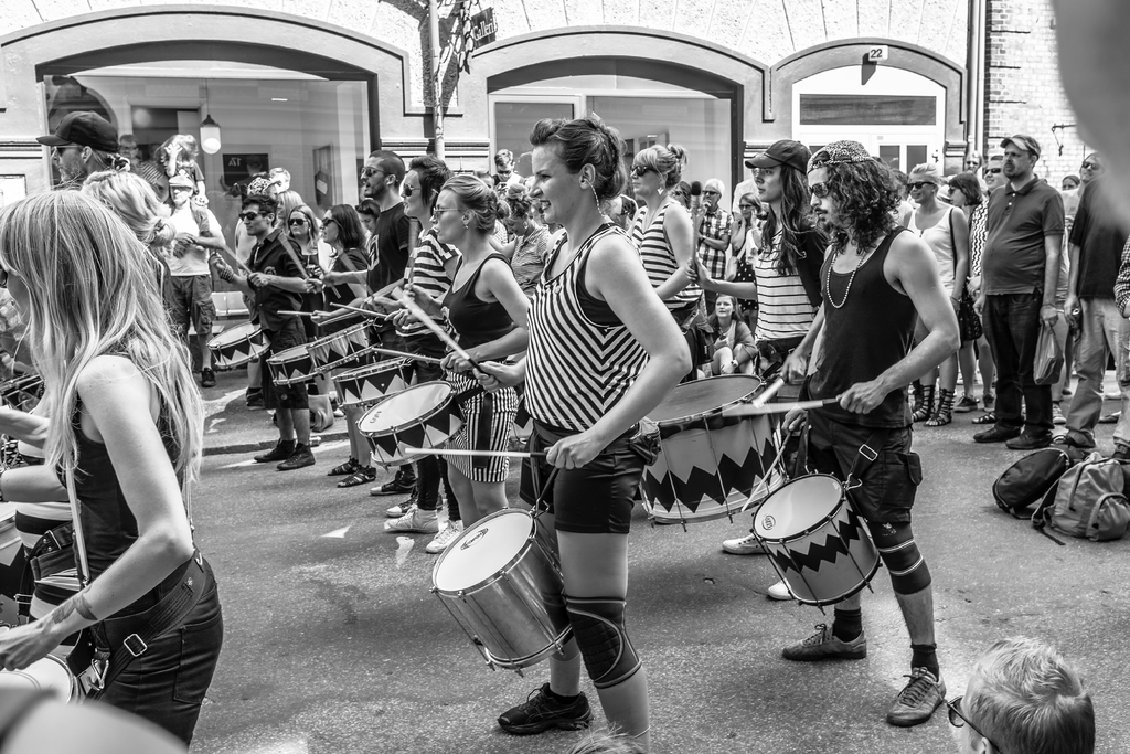 Eine Gruppe von Menschen, die musikalische Instrumente im Freien spielen, vor einer geschlossenen Glastür mit einem Licht im Hintergrund.