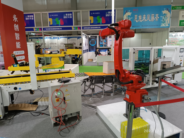 Gruppe von Robotern auf einem Tisch in einer Fabrikumgebung umgeben von Maschinen, Kabeln, beschrifteten Platinen und beleuchteten Komponenten, mit Menschen im Hintergrund.