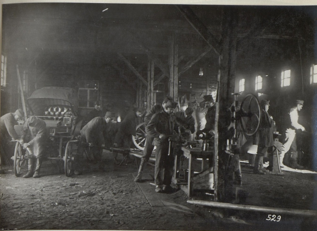Schwarz-weißes Bild von Männern, die in einer Fabrik arbeiten, mit einem Fahrzeug im Hintergrund und Fenstern auf der rechten Seite.