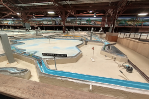 Ein großes Indoor-Wasserpark mit zahlreichen Wasserrutschen, Stangen, Texttafeln, Deckenleuchten und Wandgemälde, das als Minigolfplatz für einen spaßigen und aufregenden Erlebnis konzipiert ist.
