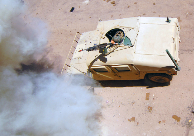 Gepanzertes Mannschaftsfahrzeug fährt eine Schotterstraße entlang, mit Rauch aus dem Fahrzeug und einer Person im Inneren.