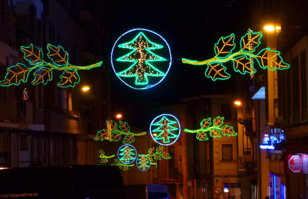 Eine nächtliche Stadtstraße, geschmückt mit festlichen Weihnachtslichtern, die Blätter und andere Schmuckstücke zeigen, mit Fahrzeugen, die an Gebäuden auf beiden Seiten vorbeifahren.