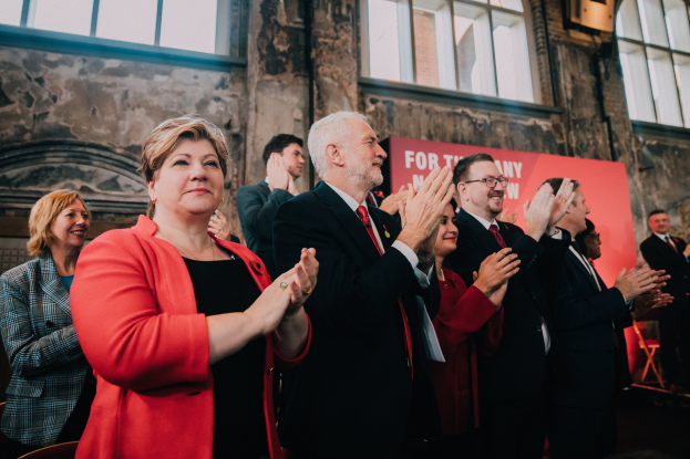 Eine Gruppe von Menschen, die vor einer Menge klatschen, mit einem Banner im Hintergrund, auf dem "Wahlsieg" steht.