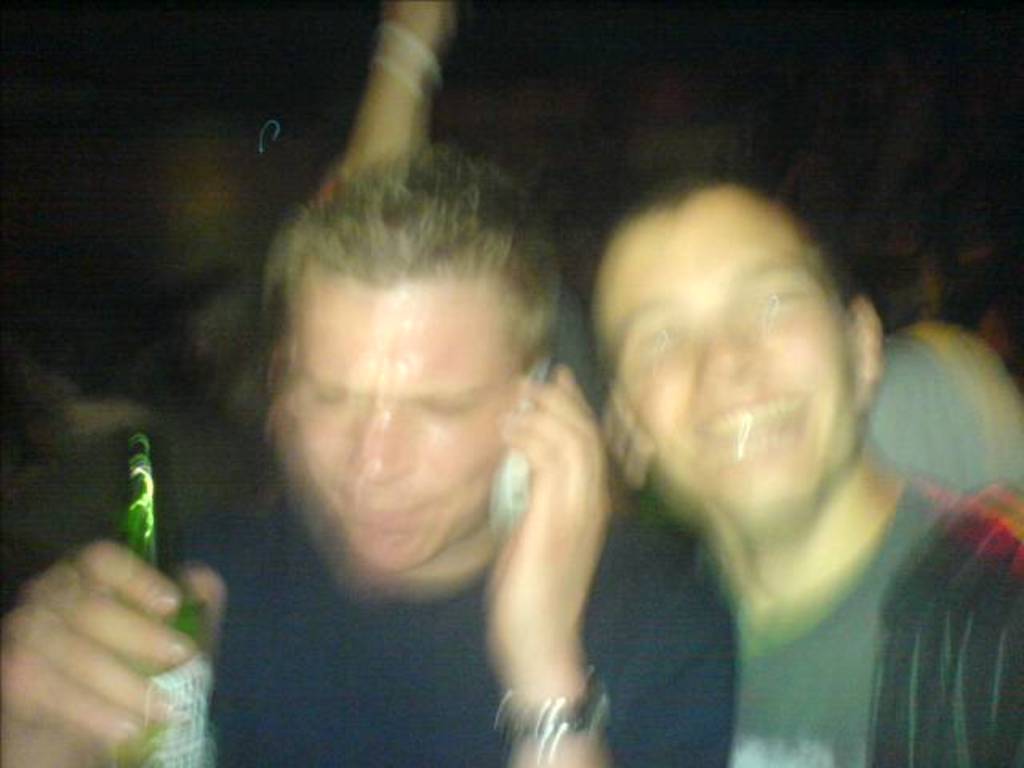 Ein Mann mit einer Bierflasche in der Hand und einem Mikrofon sprechend, neben ihm ein anderer Mann, der lächelt.