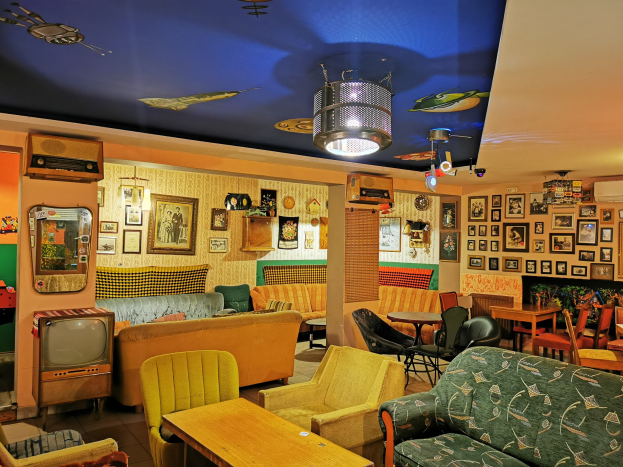 Ein unordentliches Wohn- oder Bar-Interieur mit mehreren Sofas, Stühlen, Tischen, Rahmen an der Wand, Deckenleuchten und verschiedenen Verkaufsartikeln.