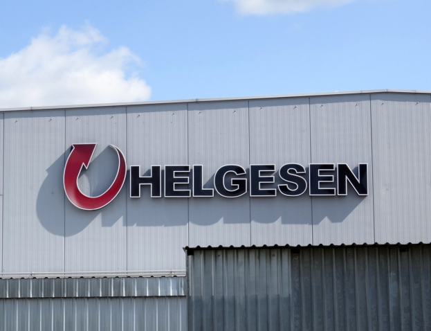 Helgesen sign auf einer Gebäudefassade mit dem Text "Helgesen investiert 1,5 Milliarden USD in den USA" vor einem bewölkten Himmel.