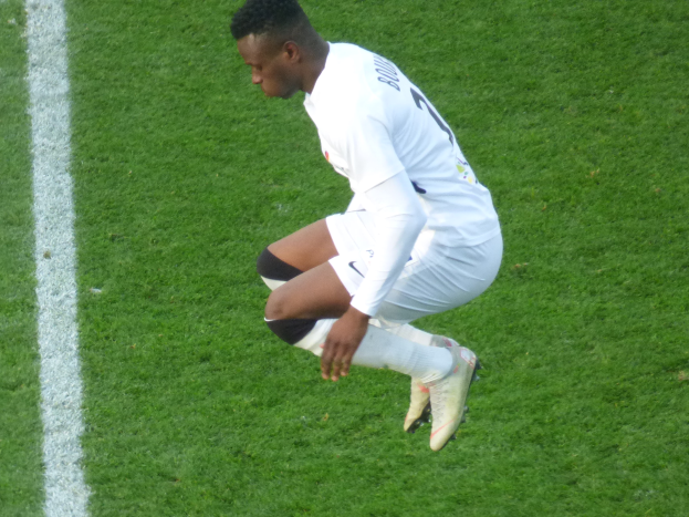 Ein Mann in weißer Uniform kniet auf einem Fußballfeld, trägt Fußballschuhe.