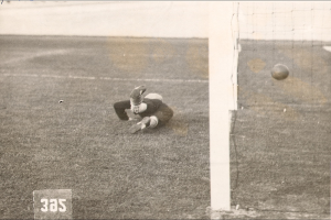 Ein Schwarz-Weiß-Foto eines Fußballspielers, der einen Ball vor einem Torpfosten mit Netz auf der rechten Seite fängt, mit Text unten.