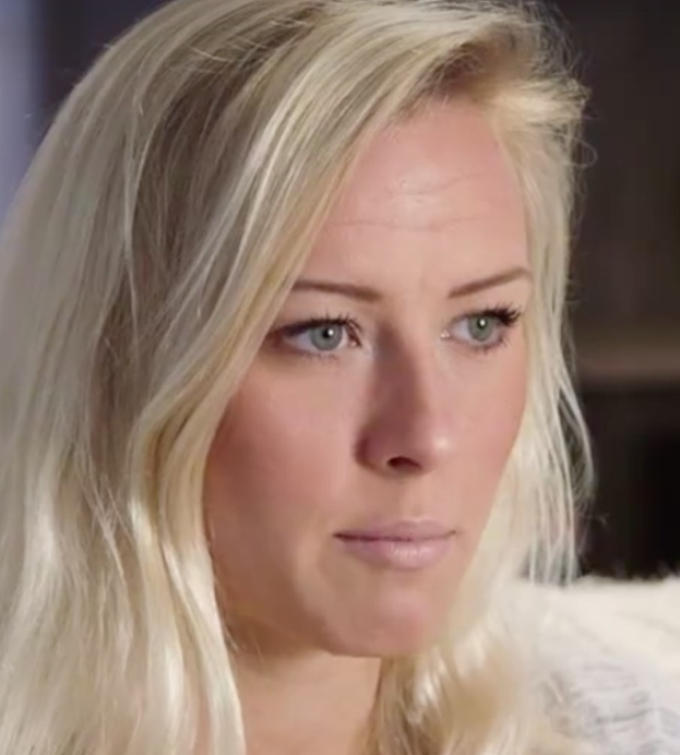 Blonde Frau mit blauen Augen im Vordergrund, Hintergrund unscharf, wirkt besorgt.