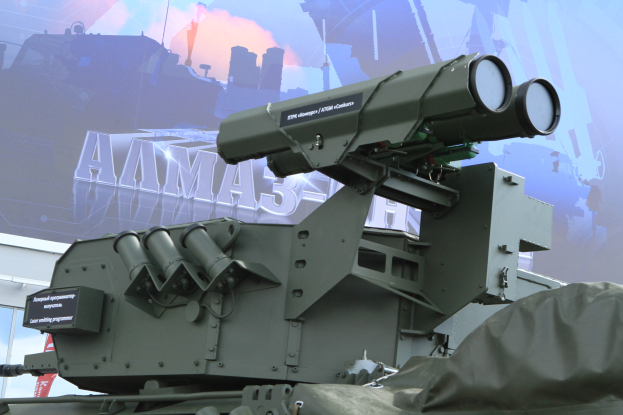 Ein militärisches Fahrzeug mit einer Flugabwehrrakete auf dem Dach, das vor einem Gebäude mit einem Banner im Hintergrund geparkt ist.