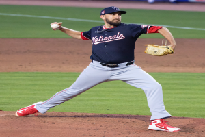 Ein Baseballspieler in einer Mütze und Handschuh wirft auf einem Rasenfeld, mit Menschen und Texttafeln im Hintergrund, die einen World-Series-Sieg für die Washington Nationals anzeigen.