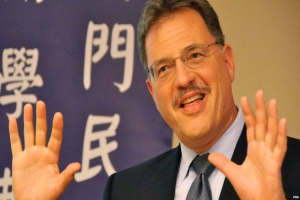 Chinas Außenminister Wang Yi, ein Mann in Anzug und Krawatte mit Brille, spricht in ein Mikrofon vor einem Banner mit Text, mit einer Wand im Hintergrund.