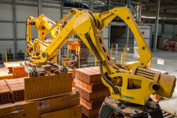 Ein großes Lagerhaus voller numerous boxes, Kräne, einen Zaun, Pfosten und andere industrielle Ausrüstung, mit einer Wand im Hintergrund, die auf eine größere industrielle Einrichtung hinweist.