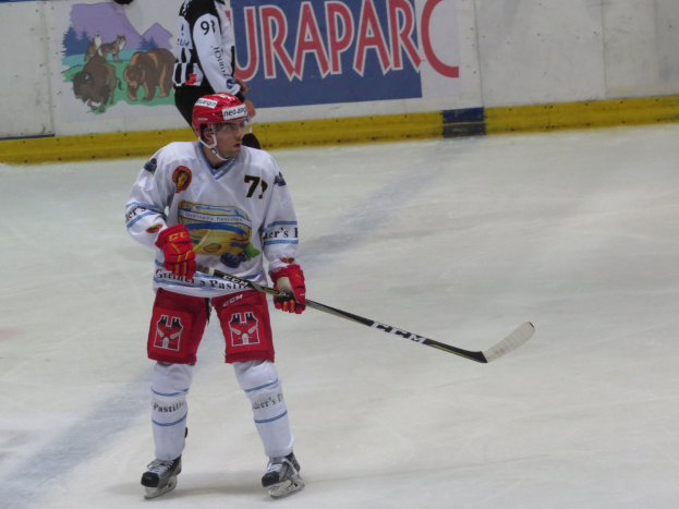 Hockeyspieler in voller Ausrüstung mit einem Stock auf dem Eis, mit einer bemalten Wand im Hintergrund.