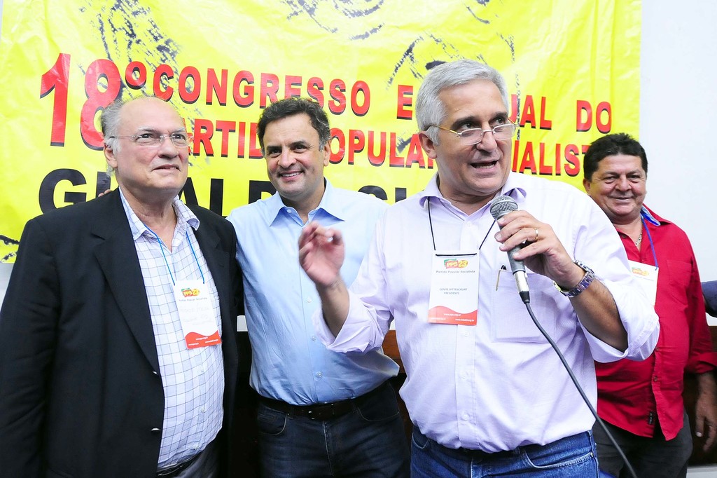 Ein Mann spricht in ein Mikrofon vor einem gelben Vorhang mit "18 Grad Kongress o" darauf, mit anderen Männern im Hintergrund.