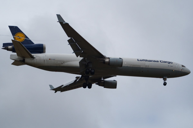 Lufthansa Cargo Boeing 777-300ER im Flug mit sichtbarem Text auf dem Rumpf, ausgebreiteten Flügeln, aktiven Triebwerken, gegen einen Himmel mit weißen Wolken.