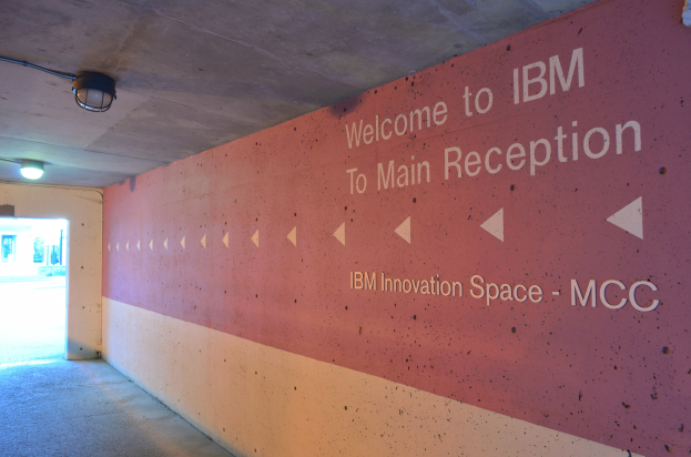 Eine Wand mit der beleuchteten Aufschrift "Willkommen bei IBM" und eine Tür im Hintergrund mit der Aufschrift "IBM Innovation Space MCC".