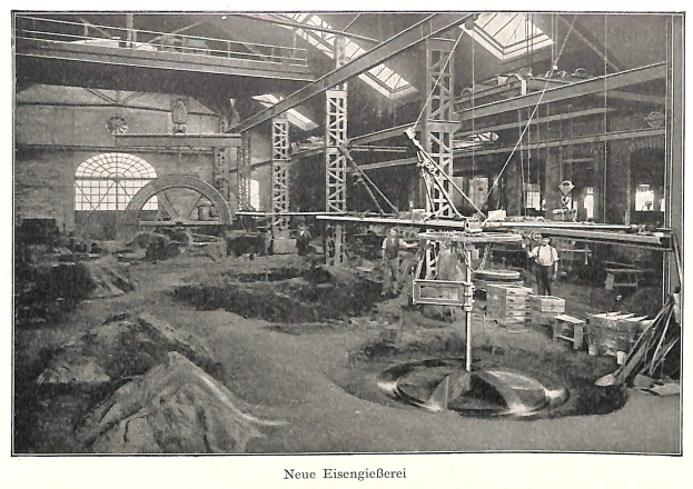 Schwarz-weißes Foto einer deutschen Fabrik aus dem 19. Jahrhundert mit Arbeitern, die an einer Maschine arbeiten, umgeben von Metallstangen und -polen, beschriftet mit "Neue Eisenglebeerei, die erste Fabrik in Deutschland."