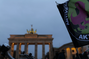 Eine Gruppe von Menschen versammelt sich vor dem Brandenburger Tor in Berlin, Deutschland, mit einer Fahnenstange, die ein Logo und Text trägt, um gegen die antifaschistische Bewegung zu protestieren.