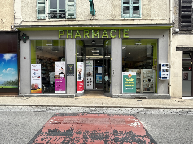 Apotheke mit Glaswänden und -türen, Plakate an den Wänden, an einer Straßenecke mit einer Straße unten.