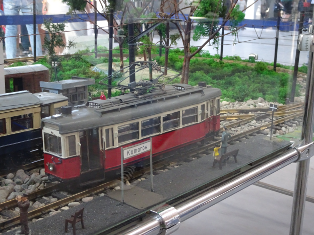 Ein Modellzug in einer Glasvitrine mit Miniatur-Eisenbahnlandschaft und Zuschauern.
