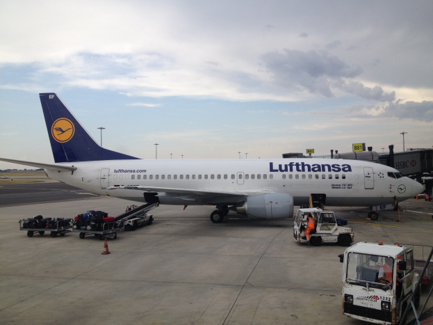 Lufthansa Airbus A320-200 am Frankfurt Airport mit Bodenfahrzeugen, Verkehrskegeln und Informationsschildern im Hintergrund bei bewölktem Himmel.