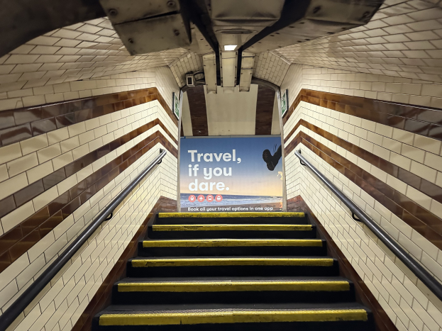 Eine Treppe in einer U-Bahn-Station mit einem 'Reise, wenn du wagst' Schild oben, flankiert von Geländern und sichtbaren Stationswänden.