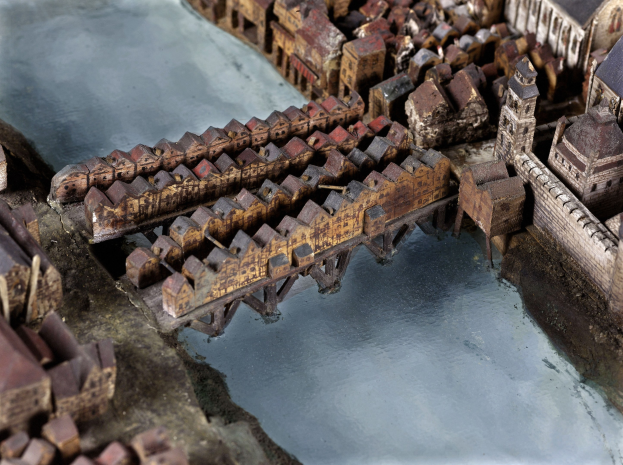 Ein detailliertes Miniaturmodell einer Stadt mit einem Fluss, einer Brücke und verschiedenen Gebäuden.