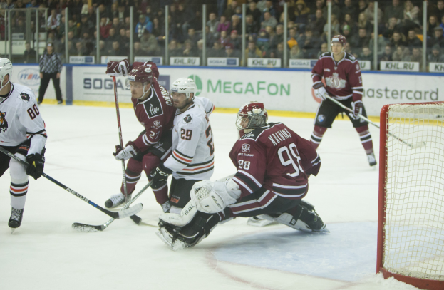 Gruppe von Menschen, die Hockey auf einem Eisstadion mit Tor auf der rechten Seite spielen, tragen Helme und halten Stöcke, Zuschauer auf Tribüne mit Bannern im Hintergrund.