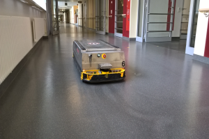 Ein Roboter, der zum Reinigen von Böden entworfen wurde, steht auf dem Boden eines Gebäudes, umgeben von Wänden, Türen, Lampen und anderen Gegenständen.